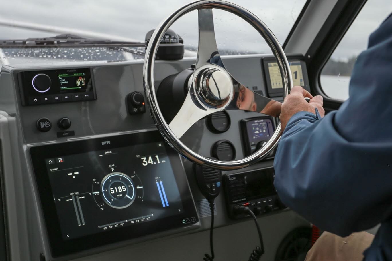 Kwigwis Adventures boat helm featuring a modern digital dashboard with navigation and engine controls, a large steering wheel, and various monitoring instruments. The cabin interior shows professional marine electronics for boat operation and safety.